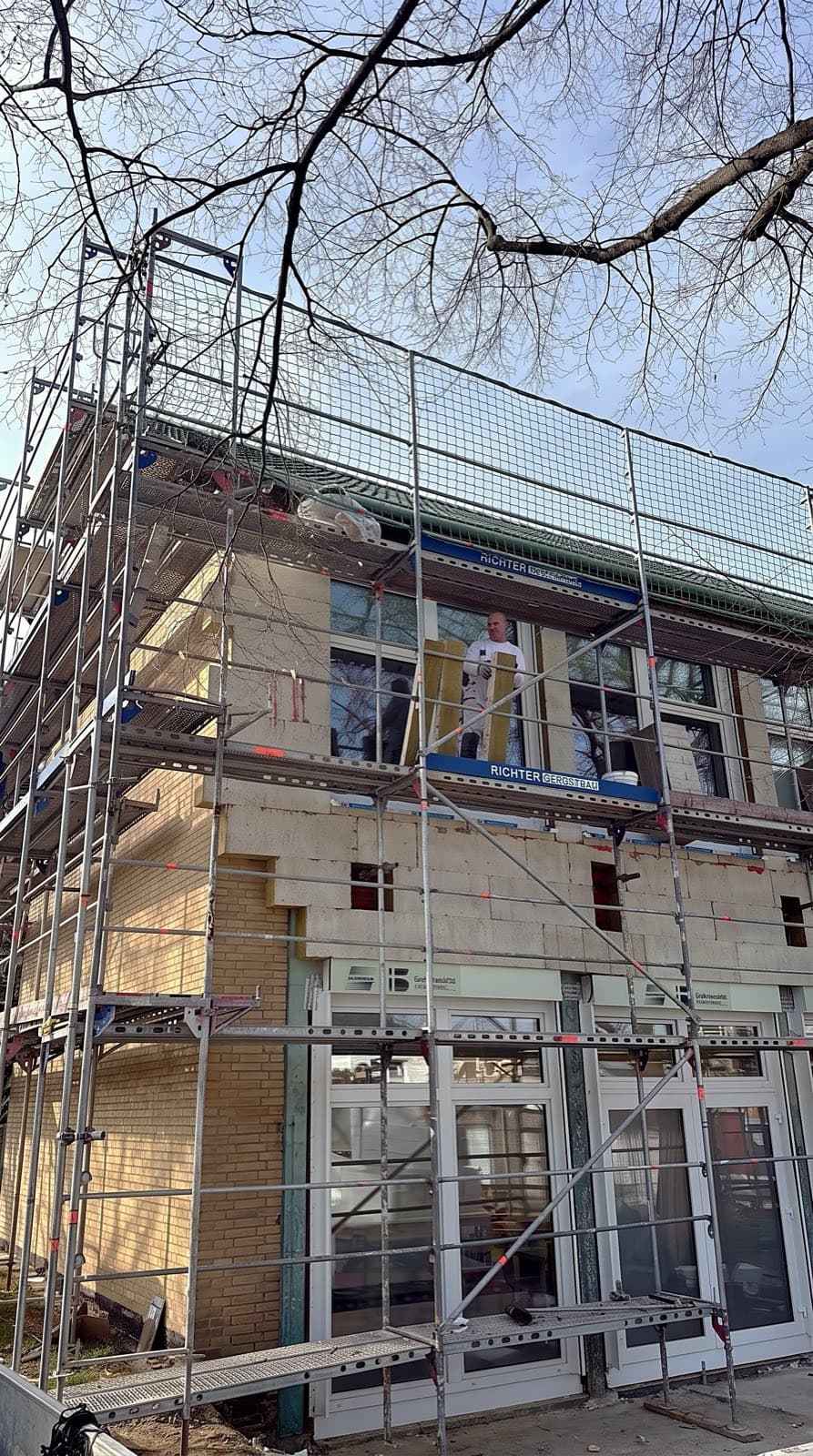 Mitarbeiter in weißer Arbeitskleidung auf dem Gerüst bei Dämmarbeiten an einer Fassade