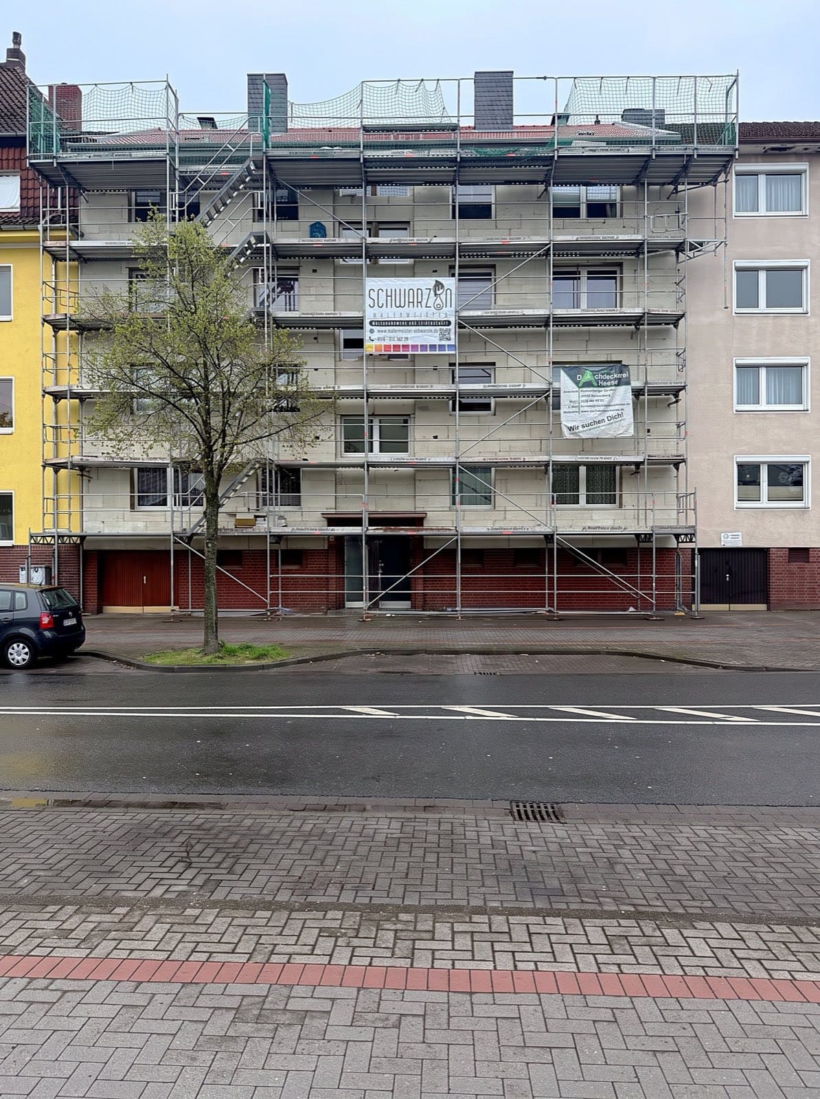 Eingerüstetes Mehrfamilienhaus mit Schwarzin-Banner am Gerüst, Straßenansicht